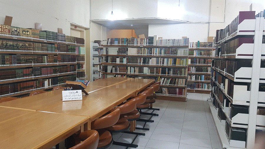 قاعة مطالعة فيها طاولات خشبية طويلة وكراسٍ بين رفوف المجلدات