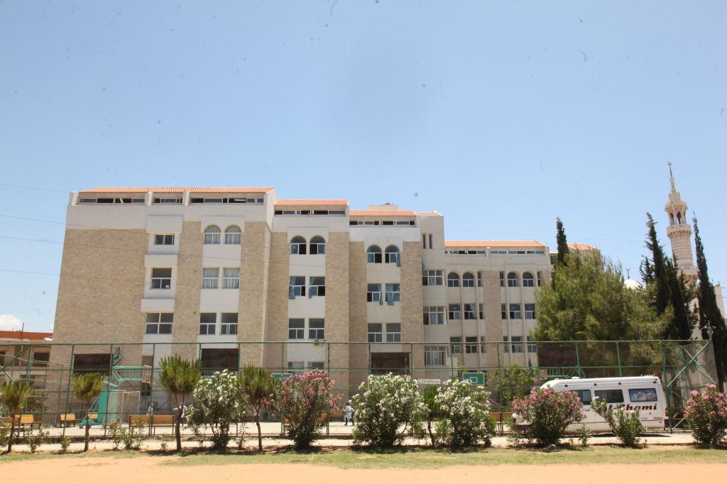 مبنى الجامعة من الحجر الفاتح، بنوافذ مقوسة وأسطح من القرميد الأحمر ومئذنة خلف الأشجار